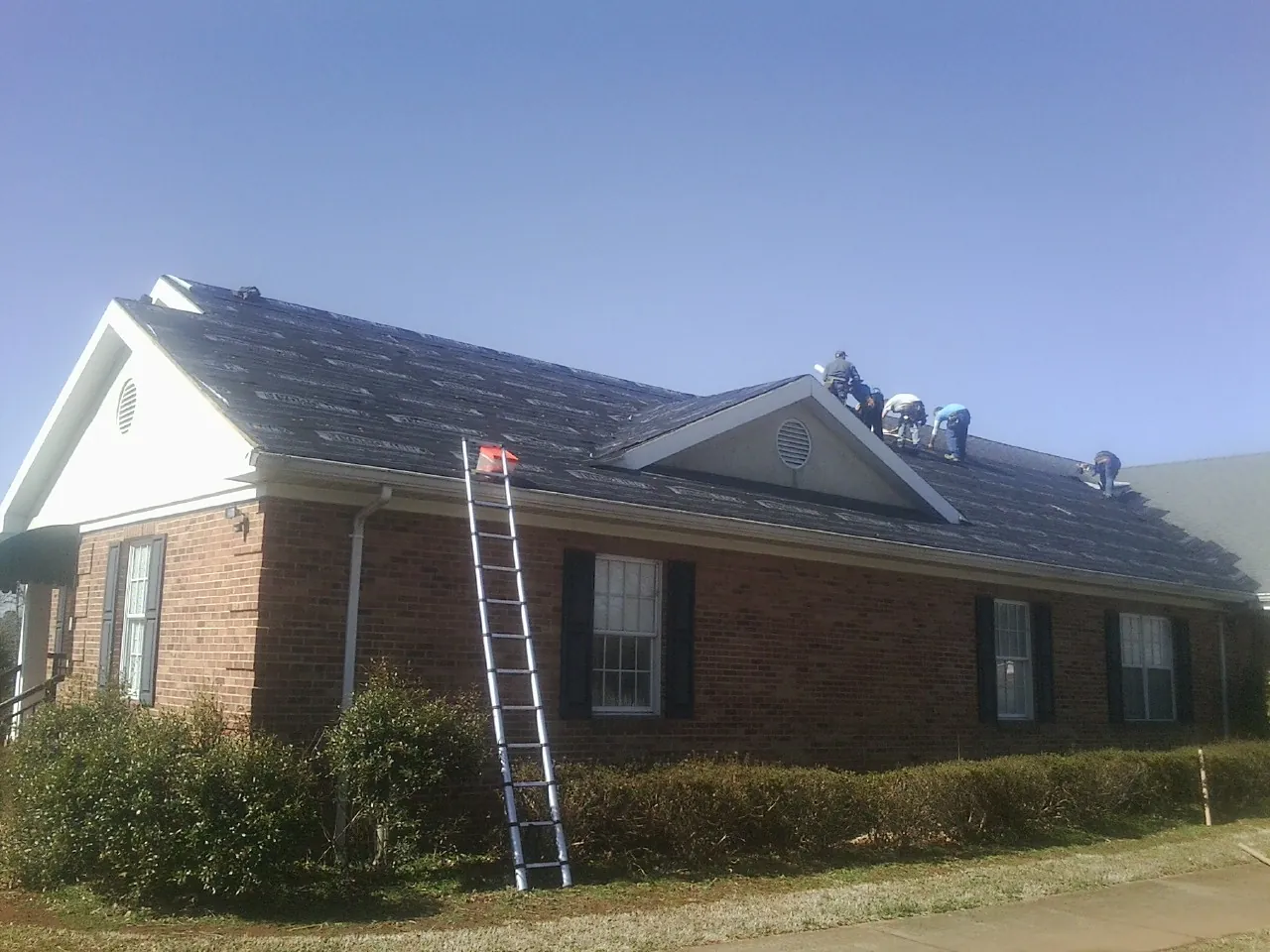 Crew tearing shingles off a brick ranch roof with a ladder set — Metal Roof Repair work by our crew in Warm Springs