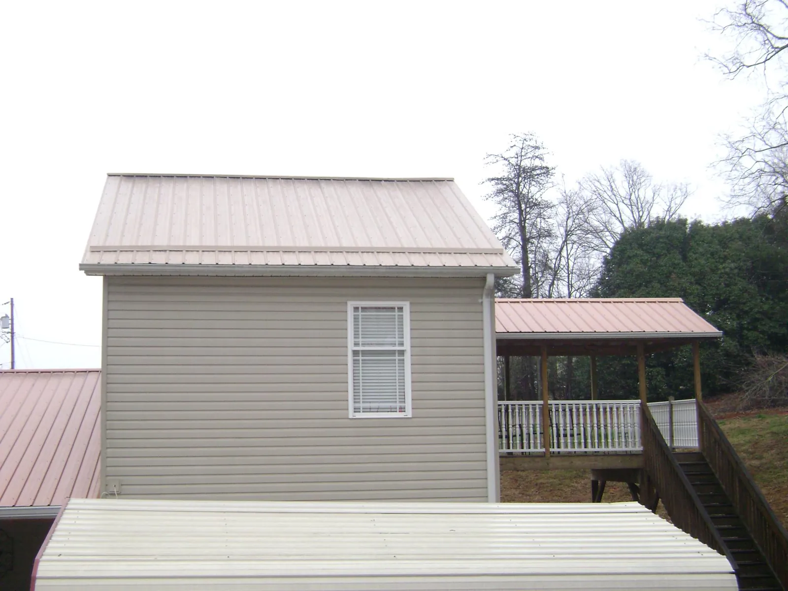 Tan metal roofs on a two story addition and attached porch, from a Roof Replacement job in Warm Springs